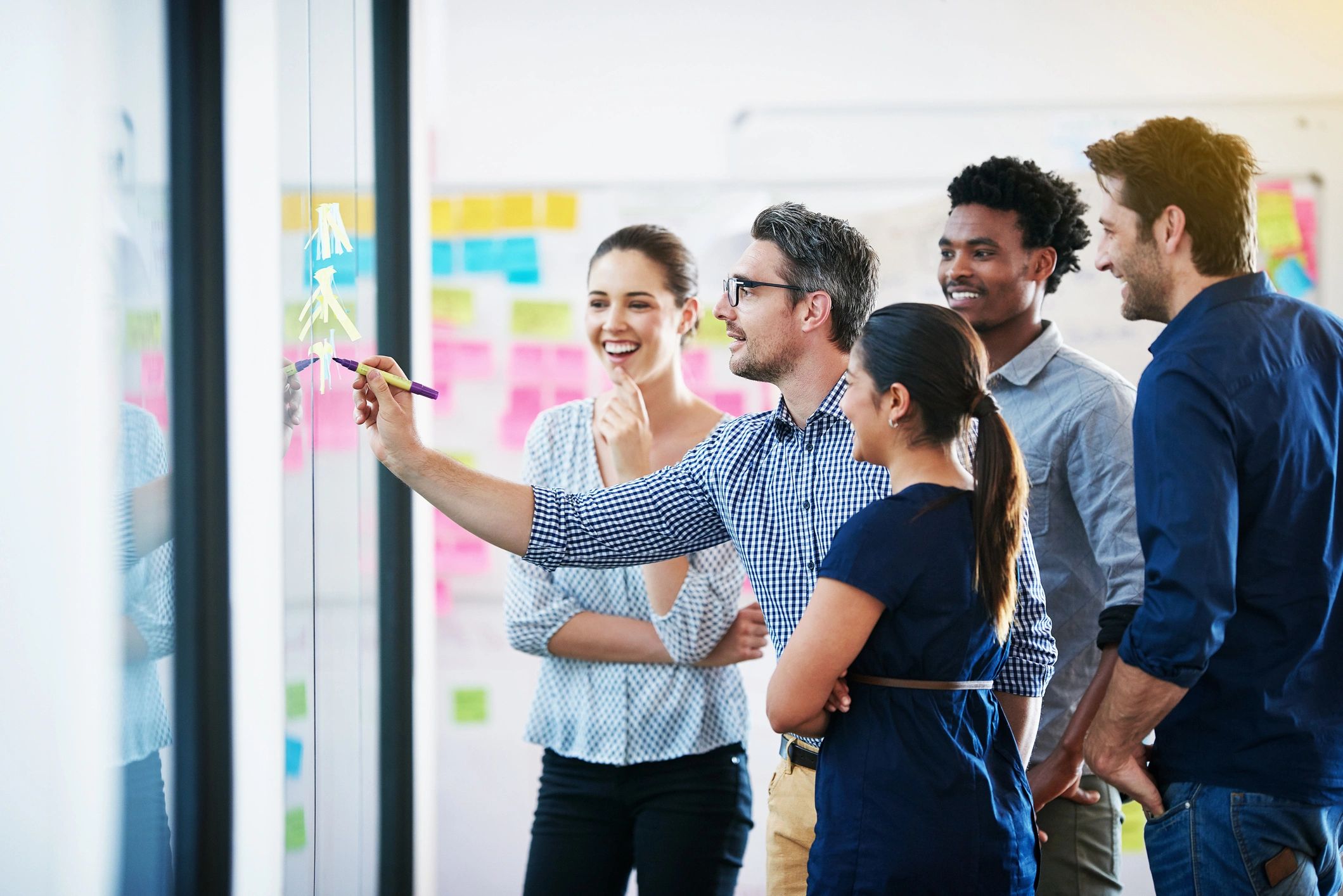 Colleagues brainstorming together on a glass wall with sticky notes